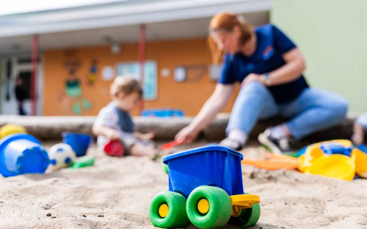 Ein Kind spielt mit einer Erzieherin im Sandkasten einer Kita.