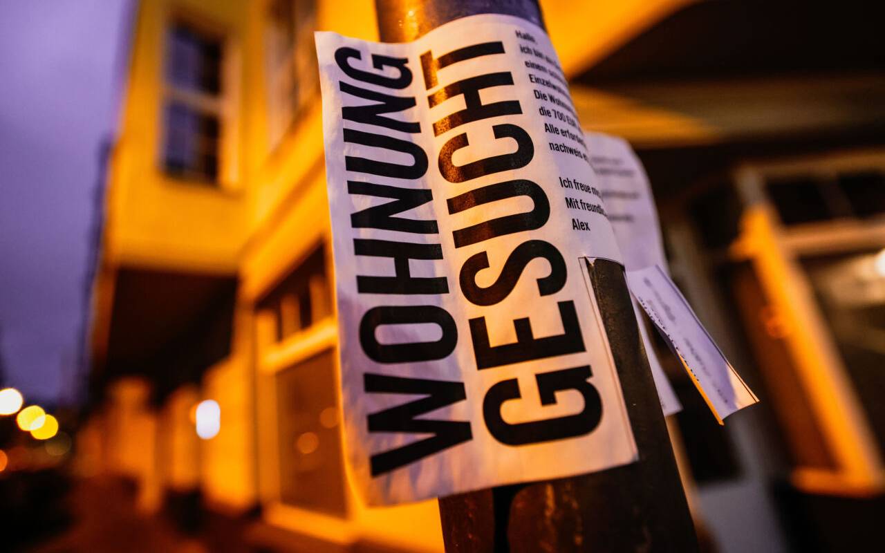Ein Zettel mit der Aufschrift "Wohnung gesucht" hängt vor Wohnhäusern.