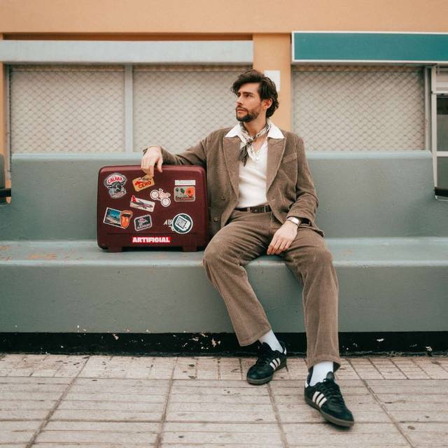 Musiker Alvaro Soler sitzt in einem Pressefoto von 2025 auf einer Bank neben einem Koffer