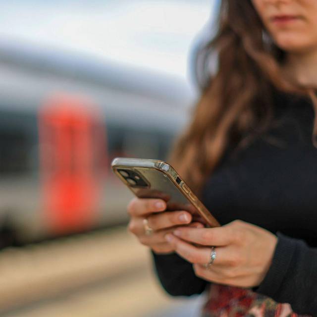 Eine junge Frau steht mit ihrem Mobiltelefon auf einem Bahnsteig