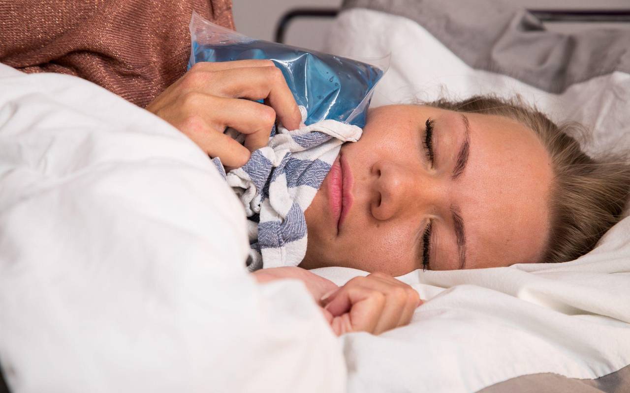 Eine Frau hält sich im Bett einen Kühlakku an die Wange