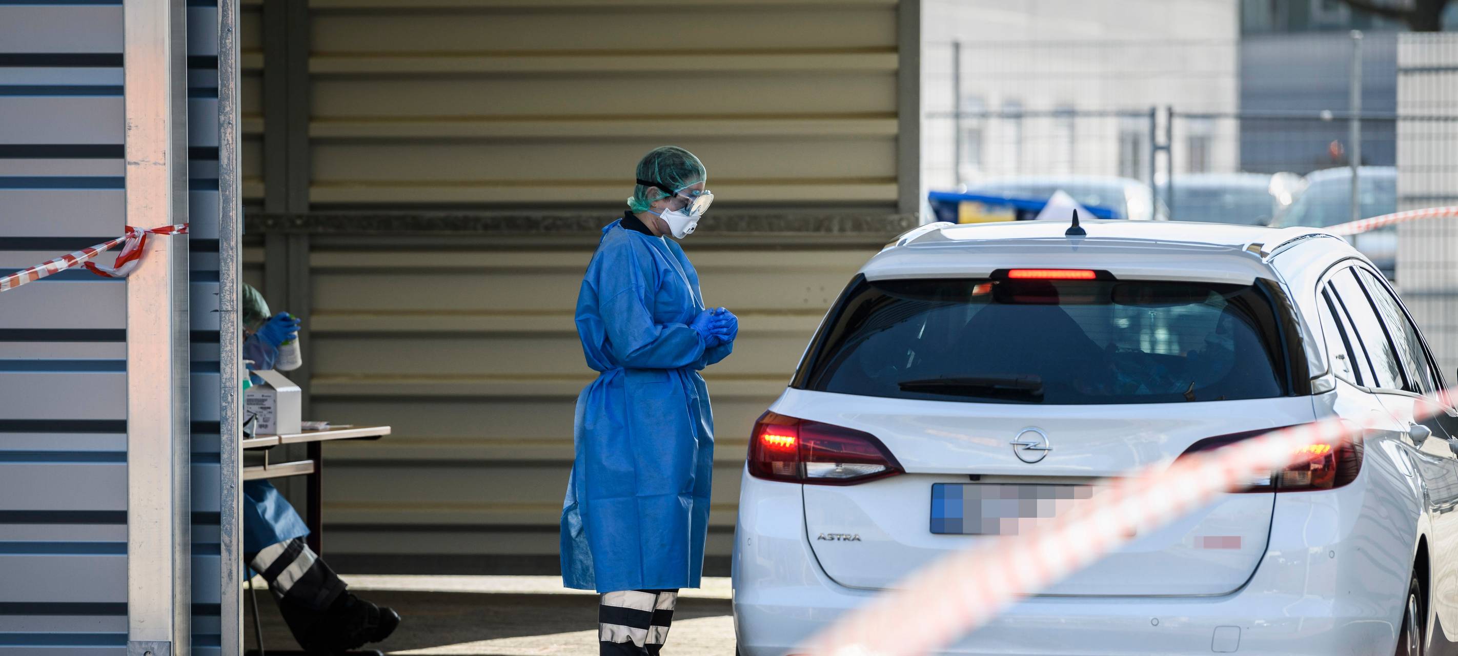 Ein DRK-Mitarbeiter in Schutzkleidung steht neben einem Auto in der provisorischen Halle der "Drive in"-Teststelle für Corona-Tests.