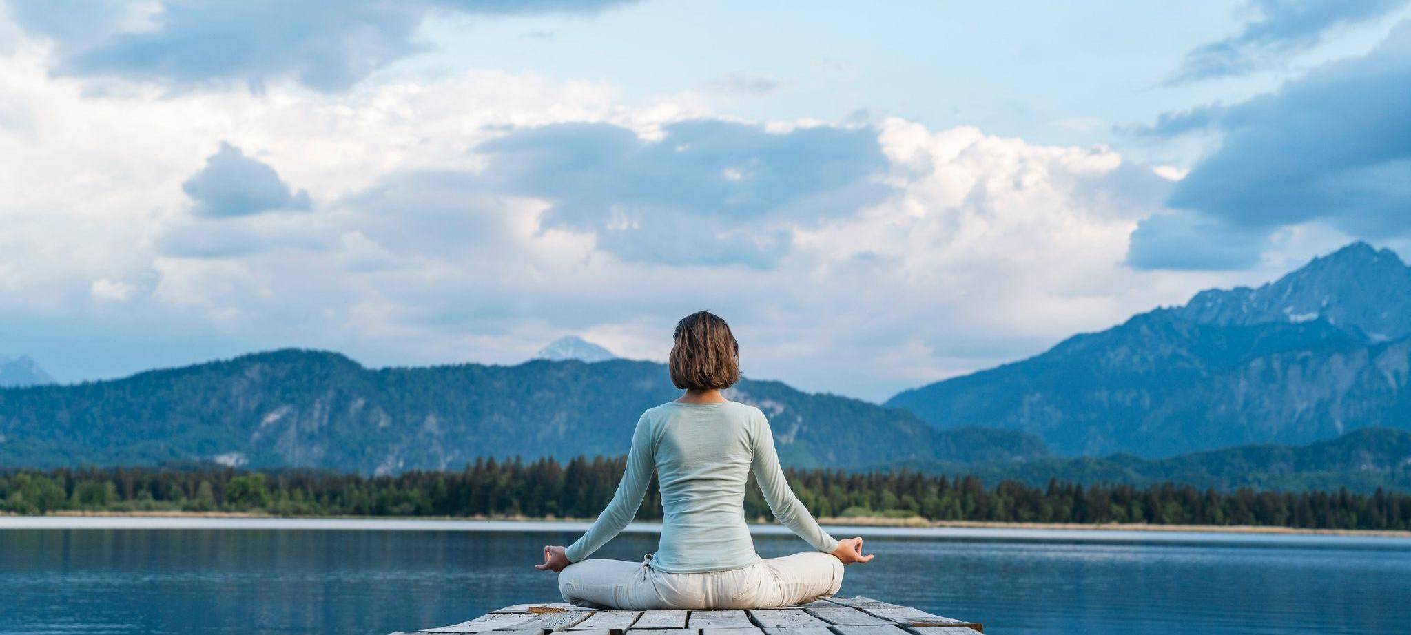 Eine Frau sitzt auf einem Steg und meditiert