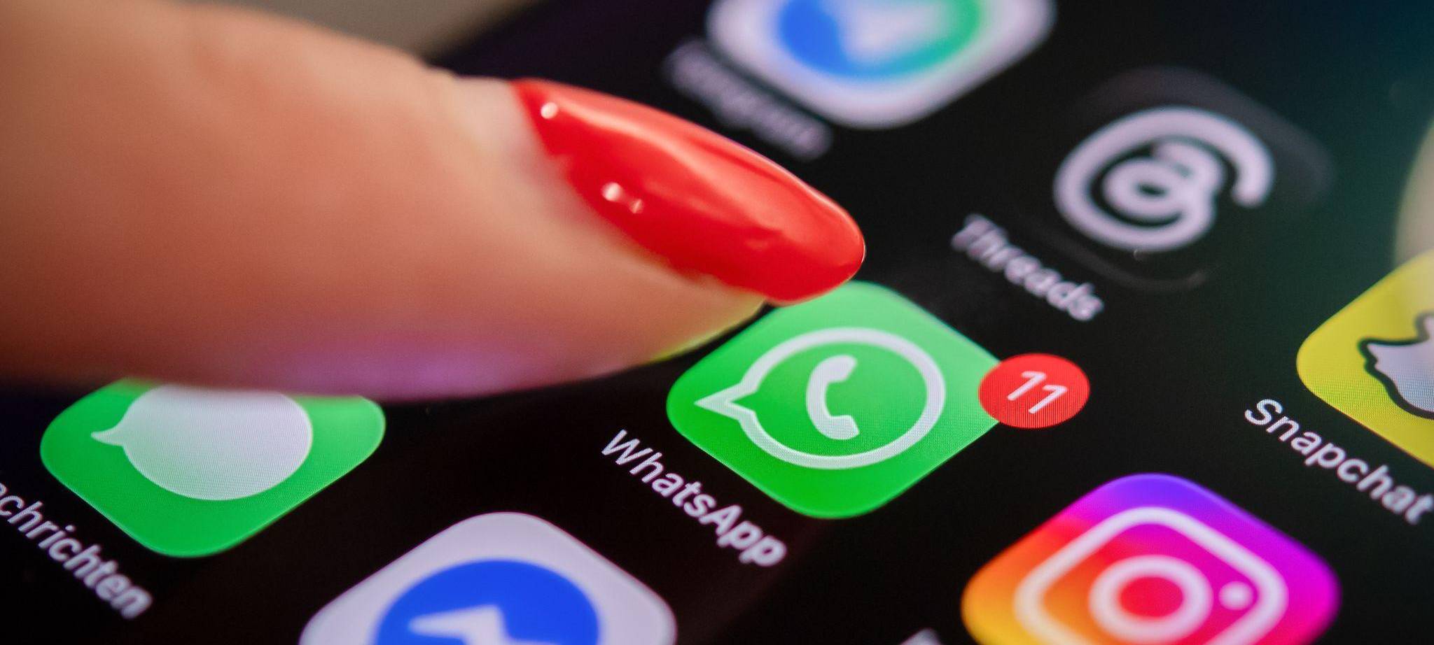 Eine Frau tippt auf einem Smartphone auf das WhatsApp-Symbol