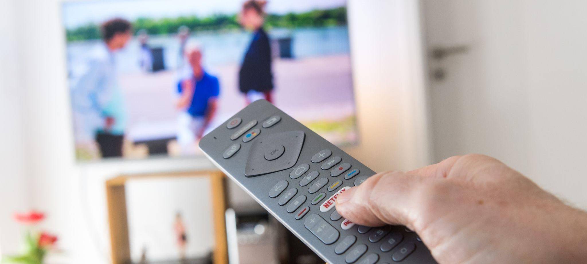 Eine Frau hält eine Fernbedienung vor einem Fernseher